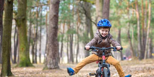A young boy in a blue helmet riding a bike in a forest.